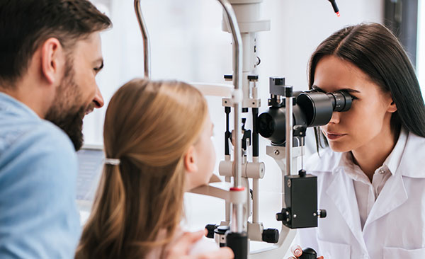 Optometrist looking at female patient's eyes though Frey slit lamp equipment